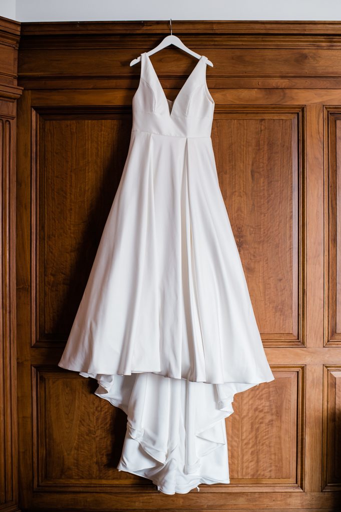 Bridal dress hanging against a wood paneled wall for Pontiac, Michigan wedding.