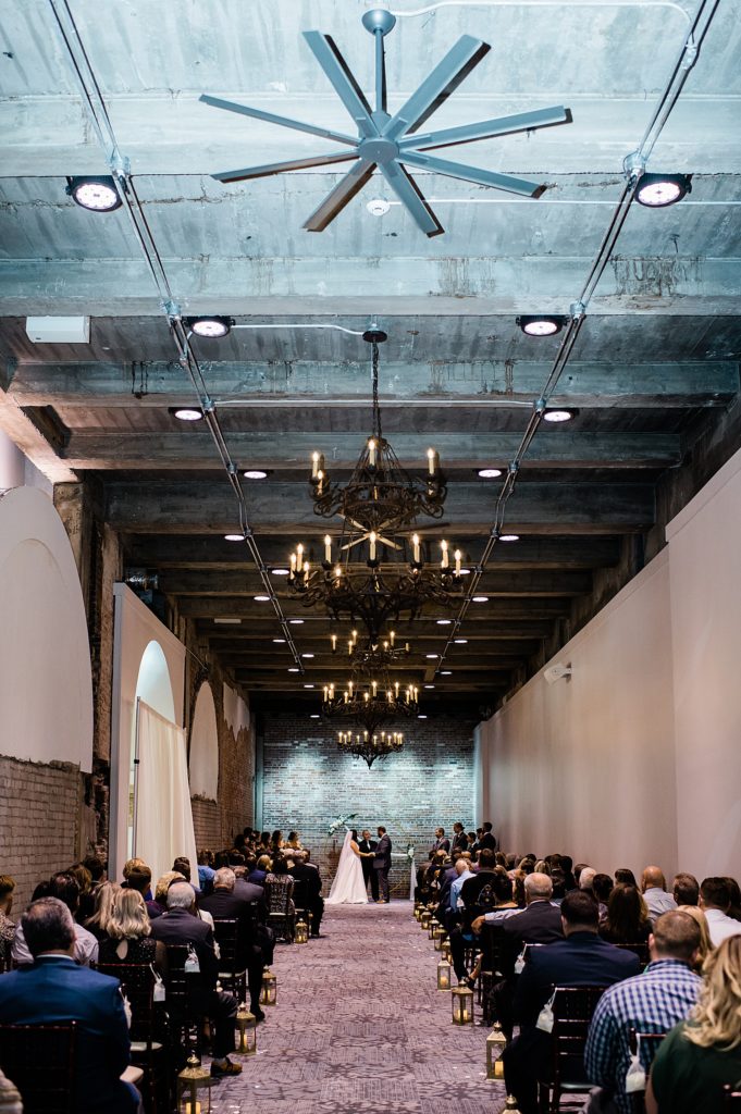 Large view shot of a wedding ceremony in a hall with chandeliers. | Wedding at The Treasury in Pontiac, Michigan.