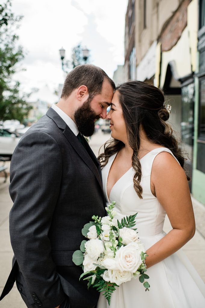 Bride and groom out on a street, putting their foreheads together and smiling after their wedding ceremony.