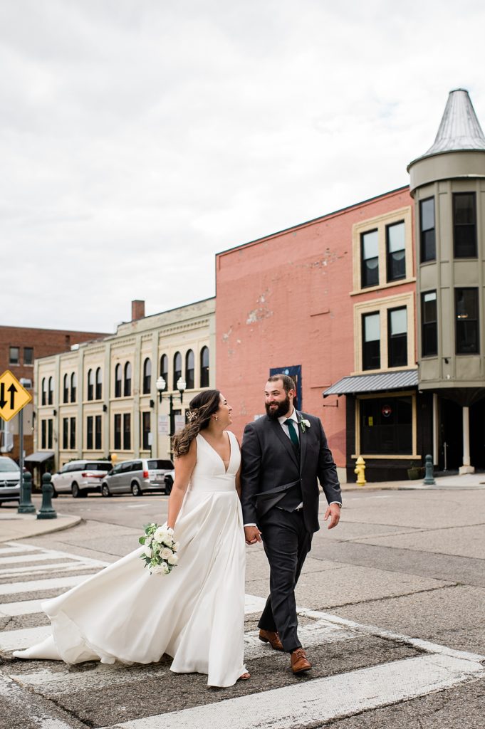 Bride and groom walking across a crosswalk, laughing and talking to each other in Pontiac. 