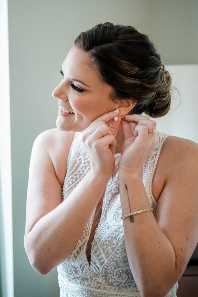 Woman in wedding dress fastening her earring. 