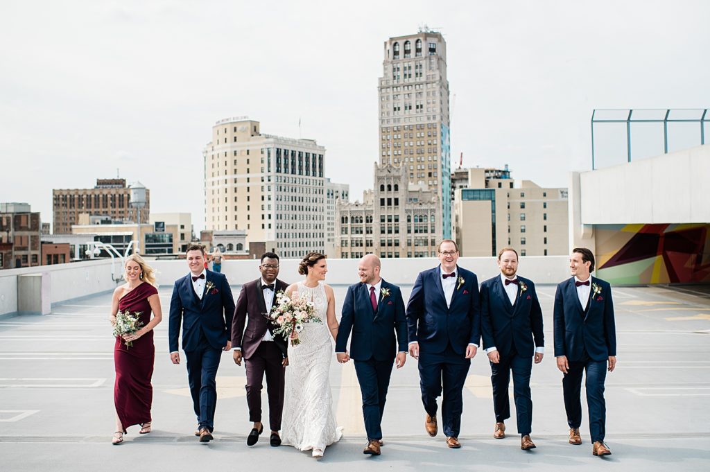 Bride and groom walking across a rooftop with their entire wedding party. 