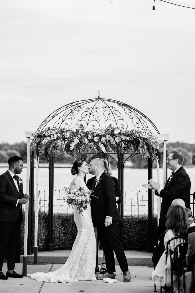 Black and white image of a bride and groom kissing at the alter. 