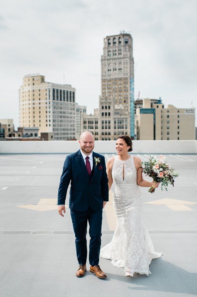 Bride and groom walking across a rooftop and smiling at each other. 