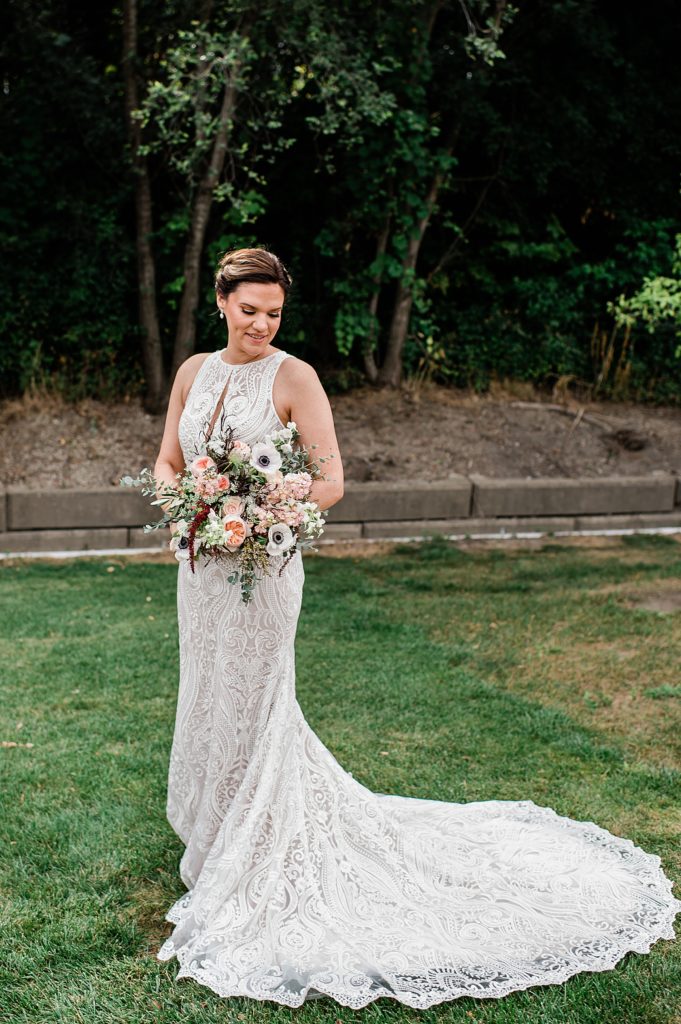 Bride standing in a garden holding her bouquet with her train wrapping around the ground.
