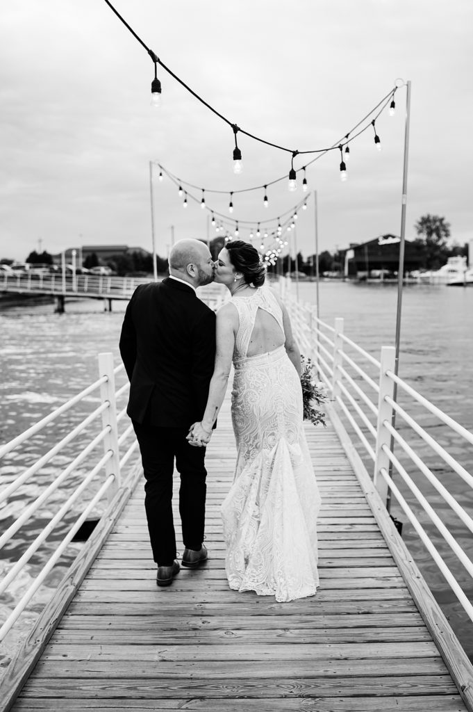 Black and white photo of a bride and groom kissing on a dock. 