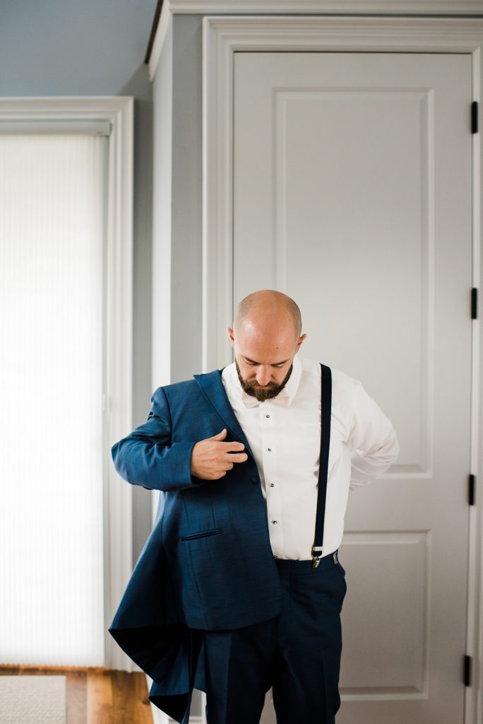 Groom putting on his blue jacket before his wedding. 