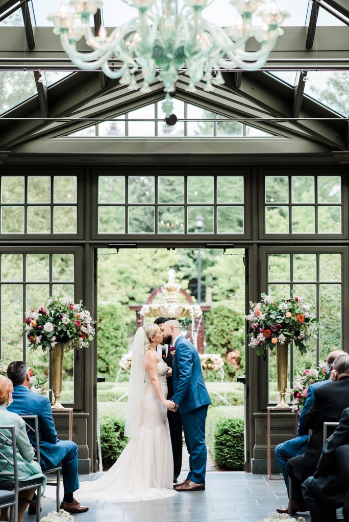 Bride and groom kissing at their wedding ceremony in the greenhouse at The Royal Park Hotel in Rochester Hills.