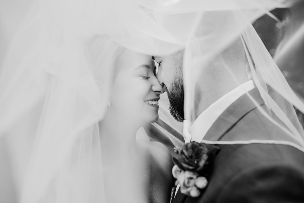 Black and white picture of a bride and groom under a veil. 