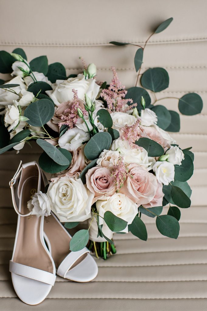 Bouquet of flowers with bridal shoes sitting next to it. 