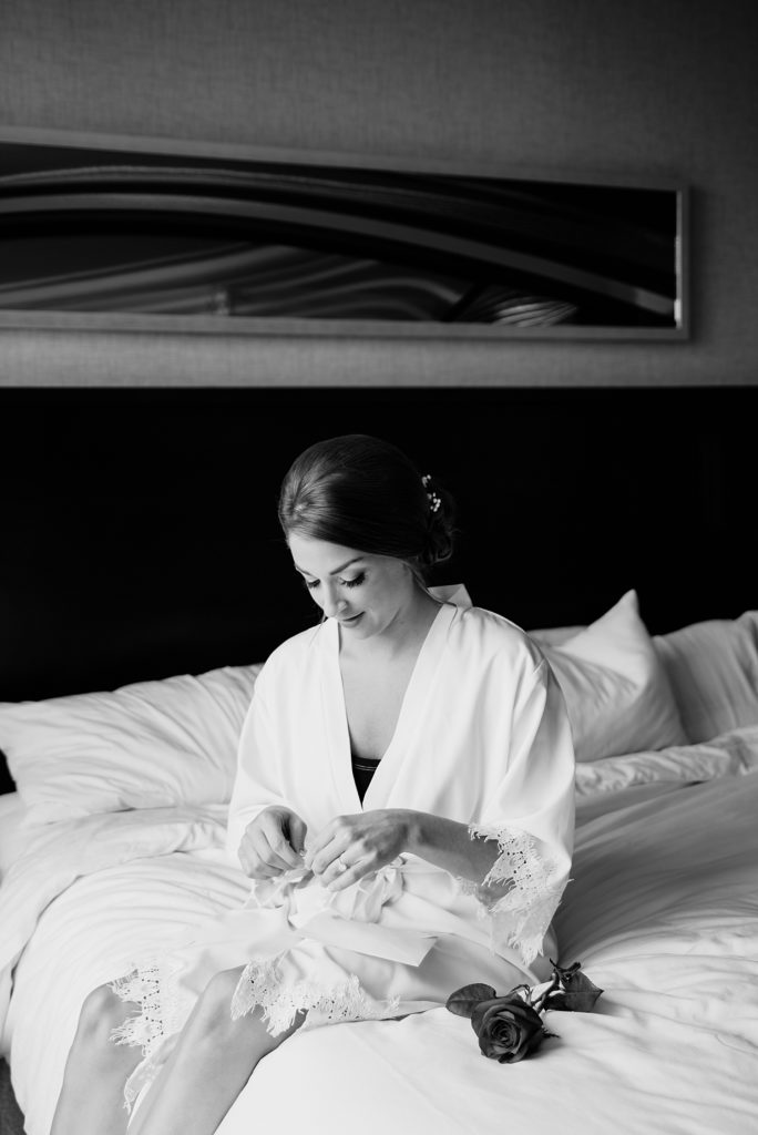 Black and white image of a bride in robe sitting on her bed before the ceremony. 