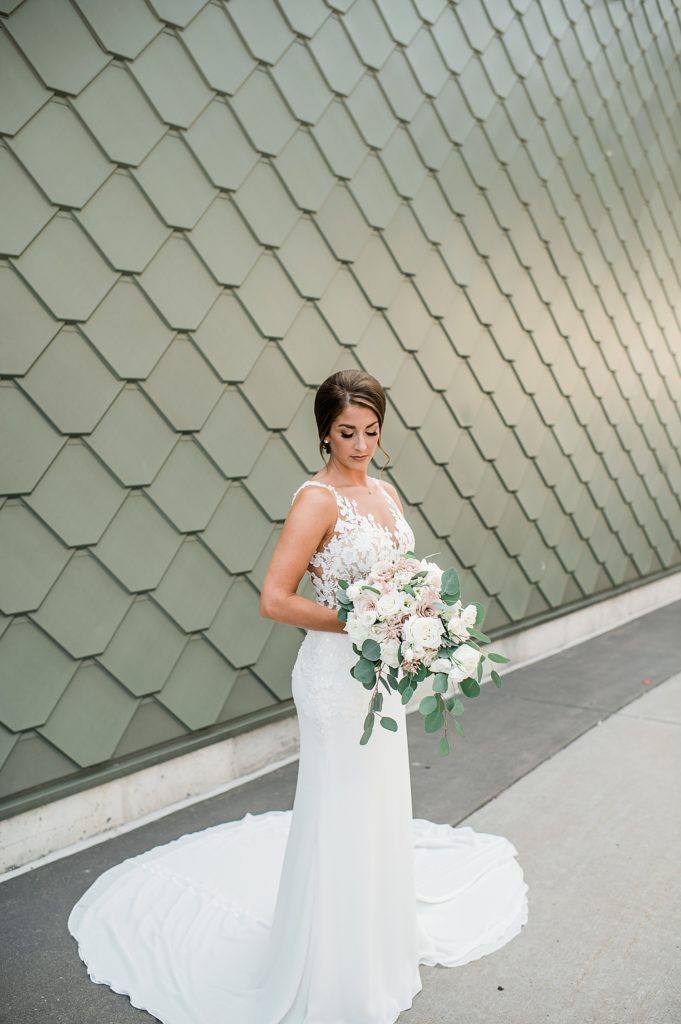 Bride looking down and holding her flowers in front of a teal tiled wall for her Waterview Loft Wedding.