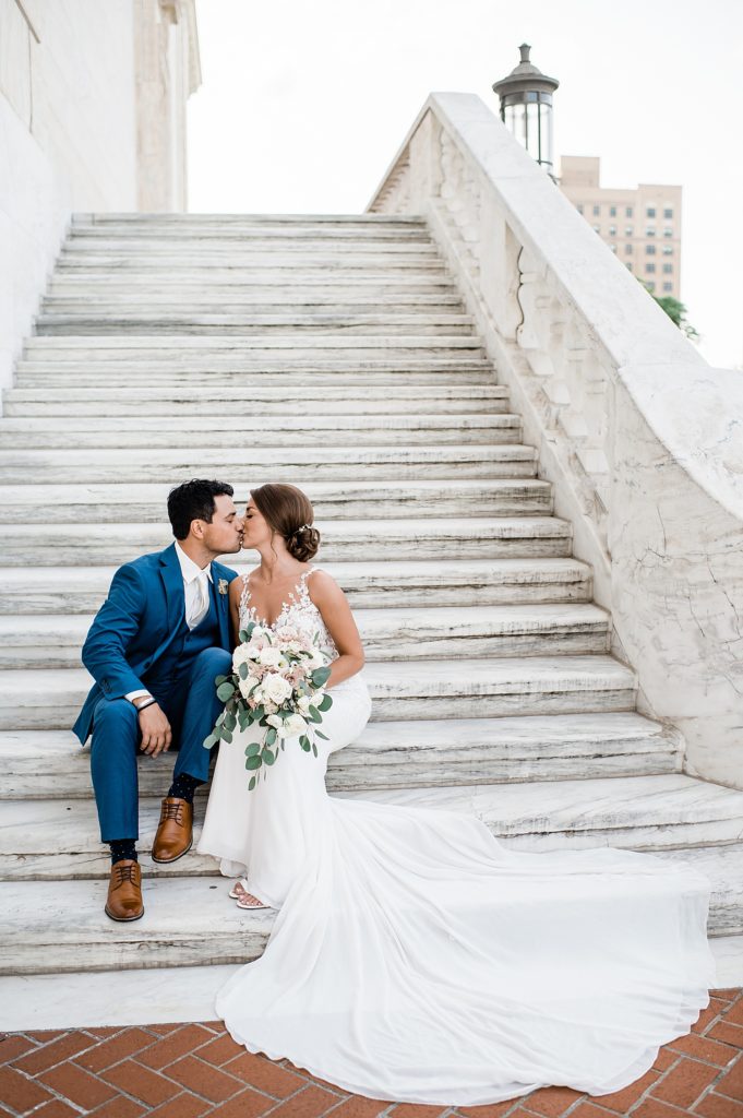 Bride and groom in blue suit sitting on large stone steps. 