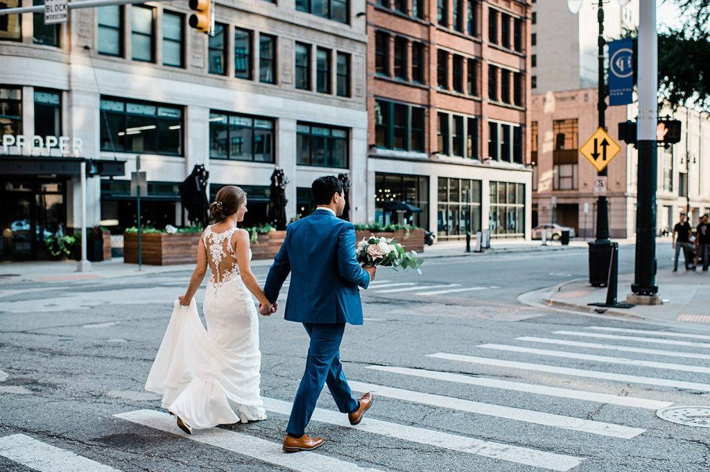 Bride and groom holding hands and walking across a side walk. 