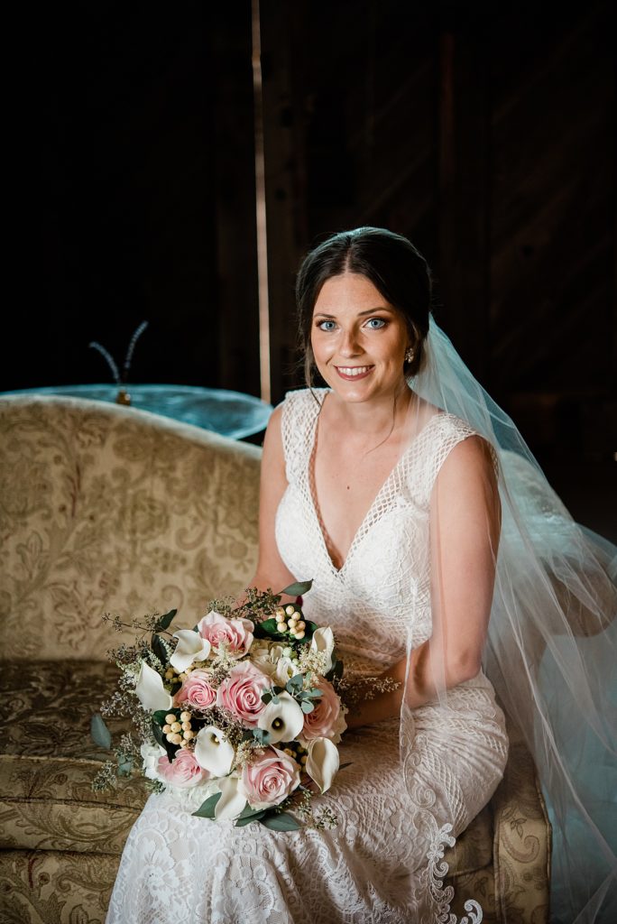 Bride sitting on an couch with her flowers, looking at the camera.
