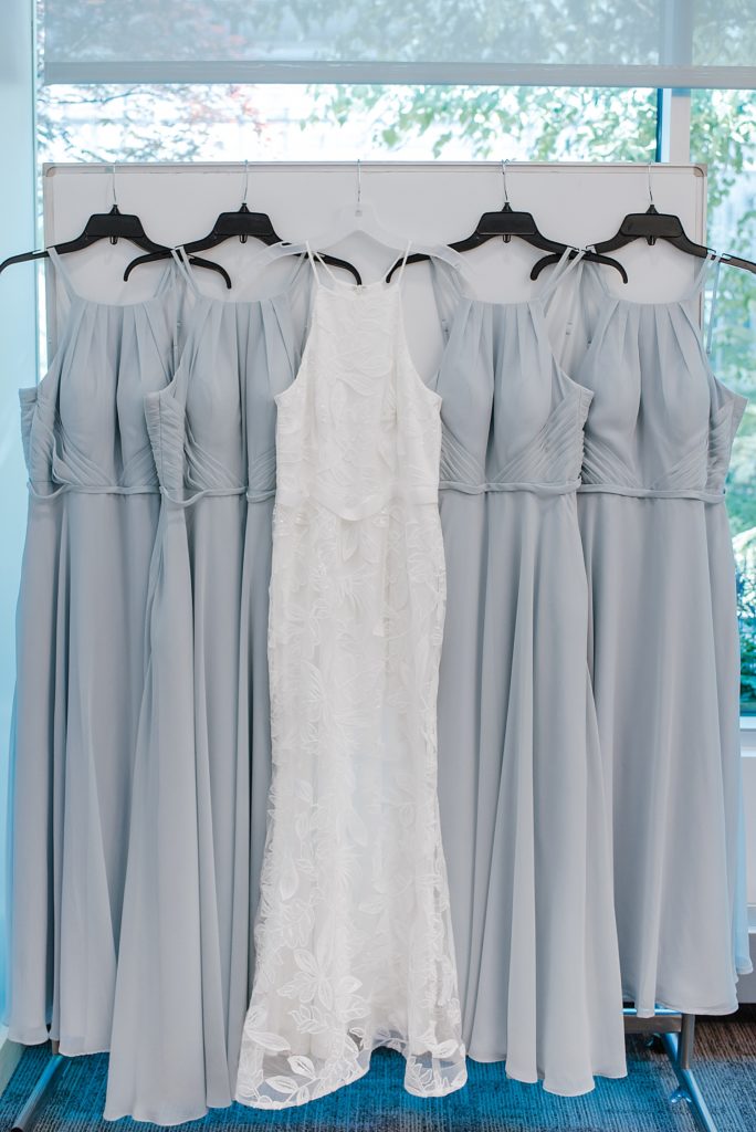 Wedding dress and bridesmaids dresses hanging against a window. 