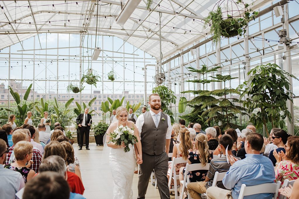 Bride and groom walking down the aisle after getting married at their greenhouse ceremony.