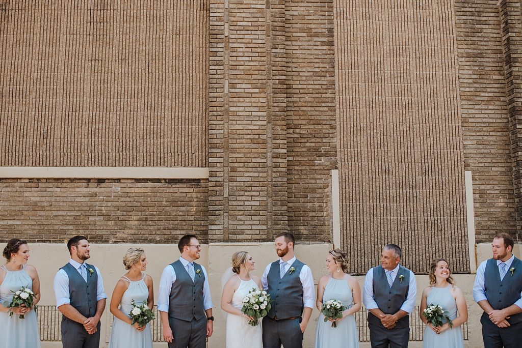 Bride and groom with their wedding party outside of a tan downtown building. 