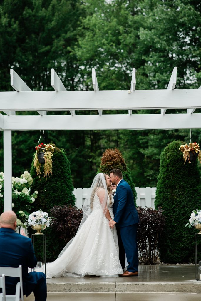 Bride and groom share first kiss at their outdoor wedding ceremony. 