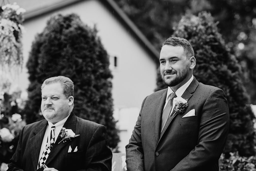 Black and white photo of groom watching his bride walk down the aisle.
