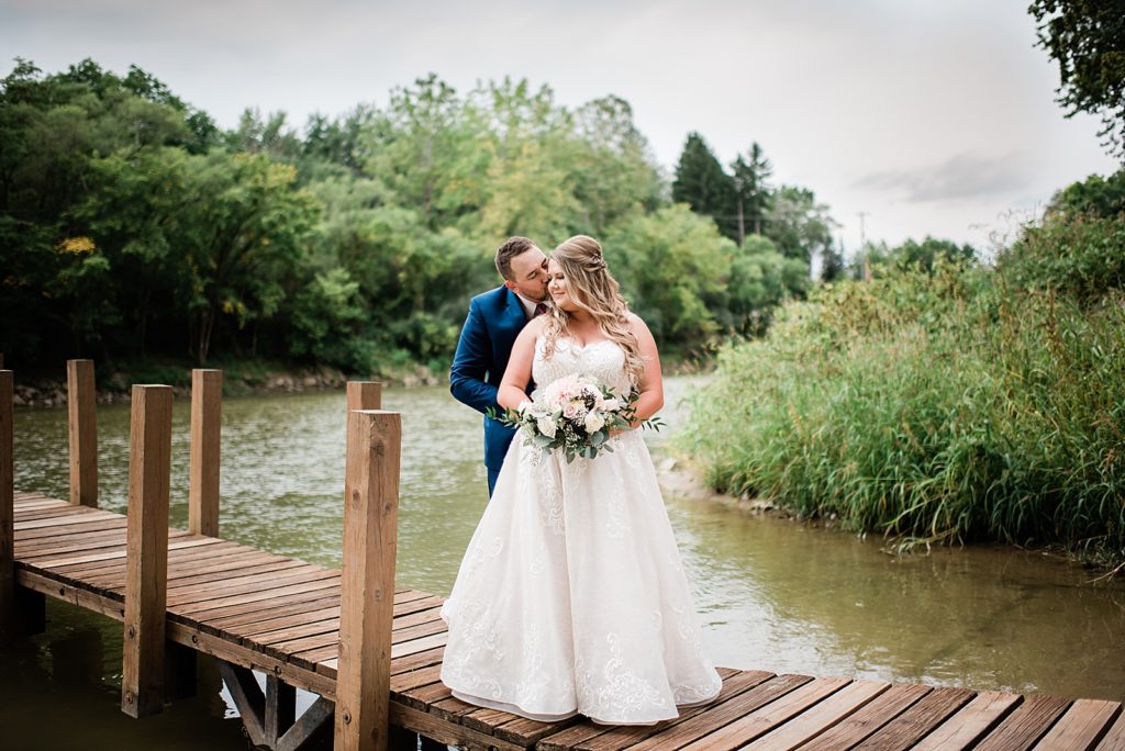 Bride and groom standing on a dock over the water. 