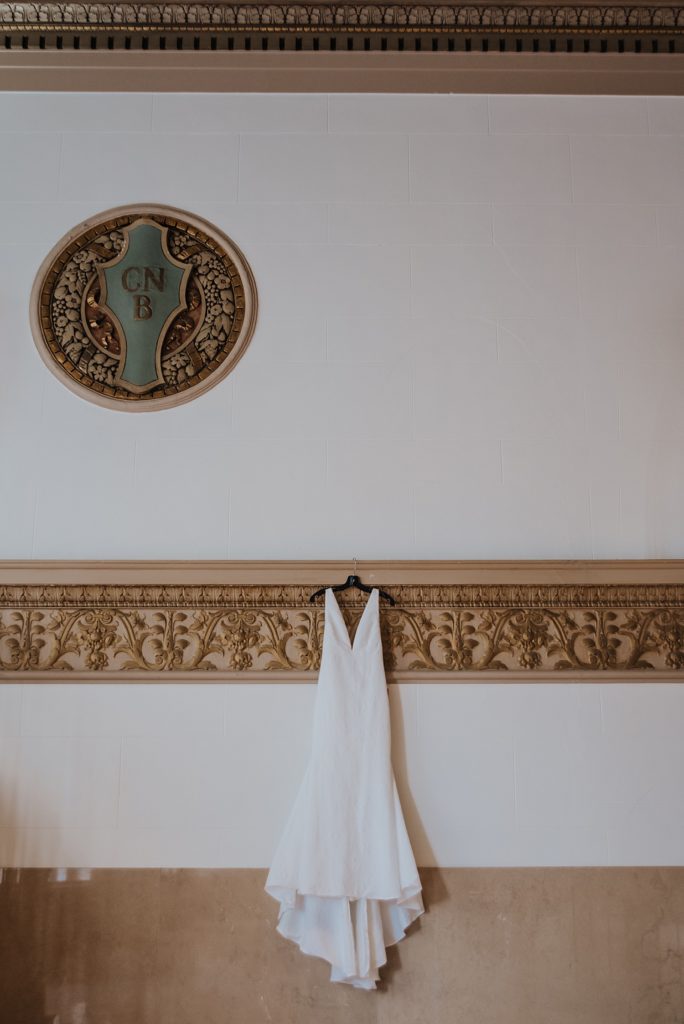A wedding dress hung against an ornate wall. 