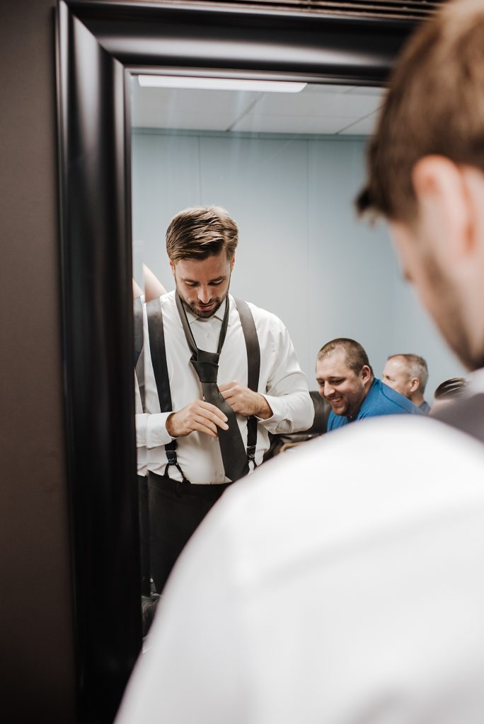 A groom fixing his tie in the mirror.