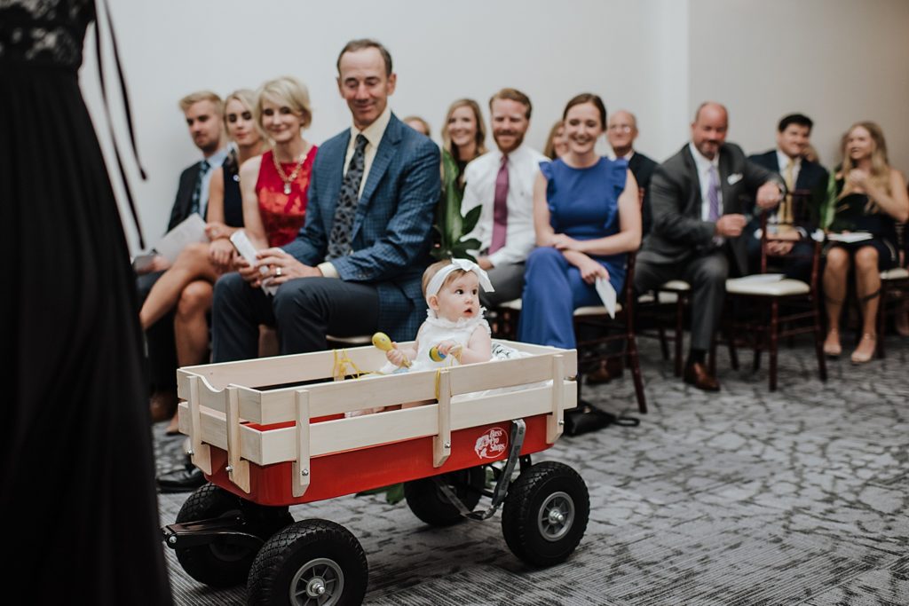 Flower girl baby being wheeled down the aisle in a red wagon.