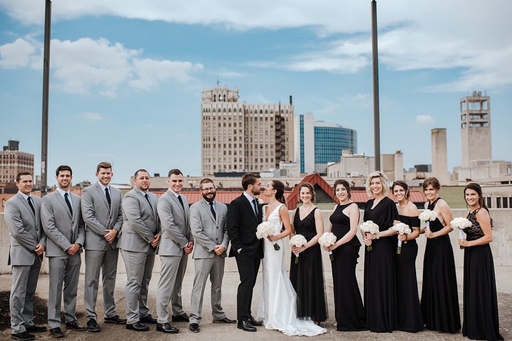 Bride and groom kissing with their wedding party around them on a rooftop. 