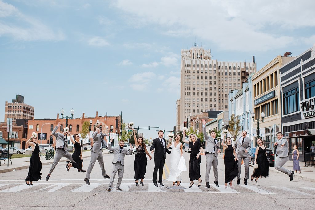 A big wedding party with bride and groom jumping on a crosswalk in the middle of Pontiac, Michigan. 