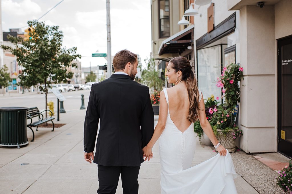 Bride and groom walking down the sidewalk in the middle of a city.