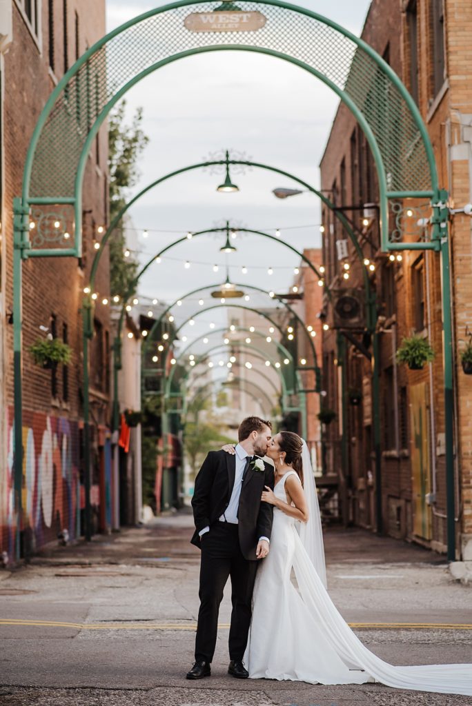 Bride and groom kissing under green arches in downtown Pontiac. 