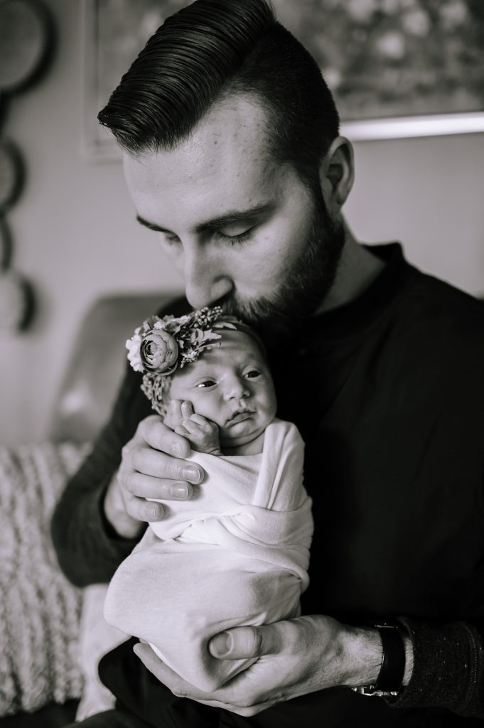 Father holding his brand new baby girl who is wearing a floral headband at their newborn photo shoot.