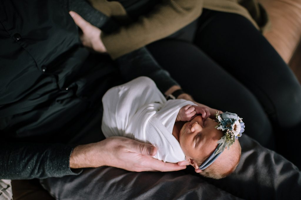 Tiny newborn in a white wrap with floral headband at her photo shoot with photographer, Brittany Emerson.