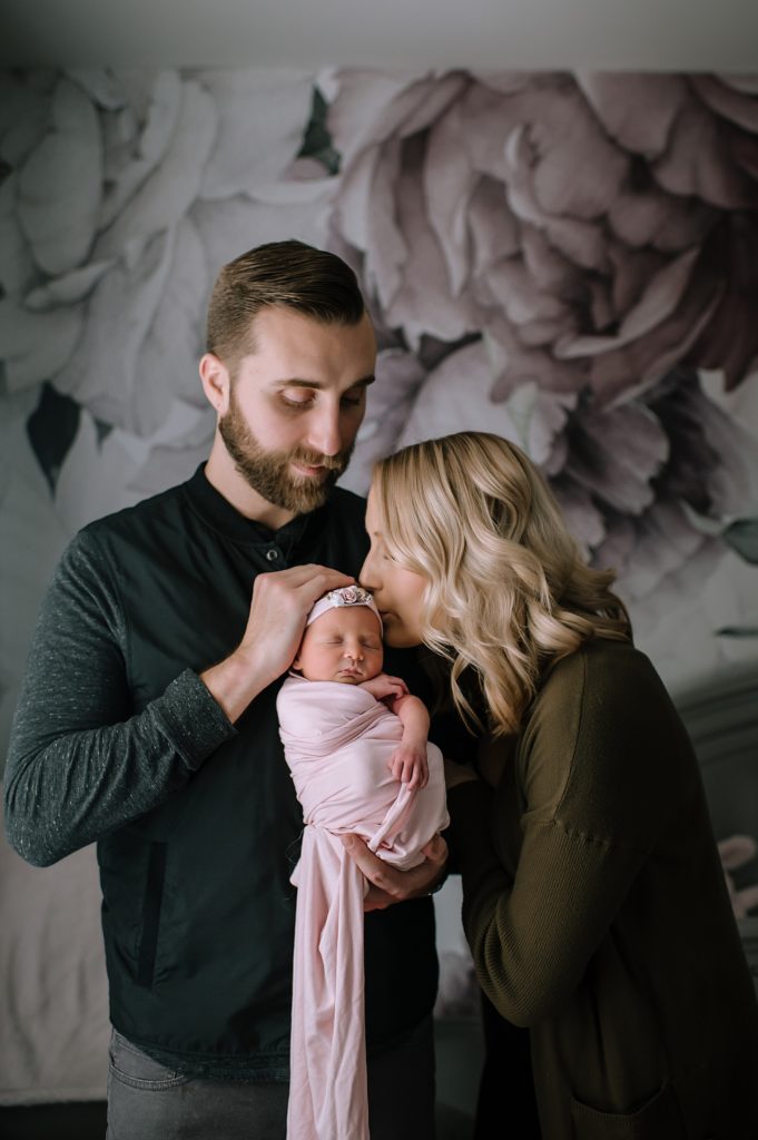 New mom and dad kissing baby in their nursery for their Michigan lifestyle newborn photo shoot. 