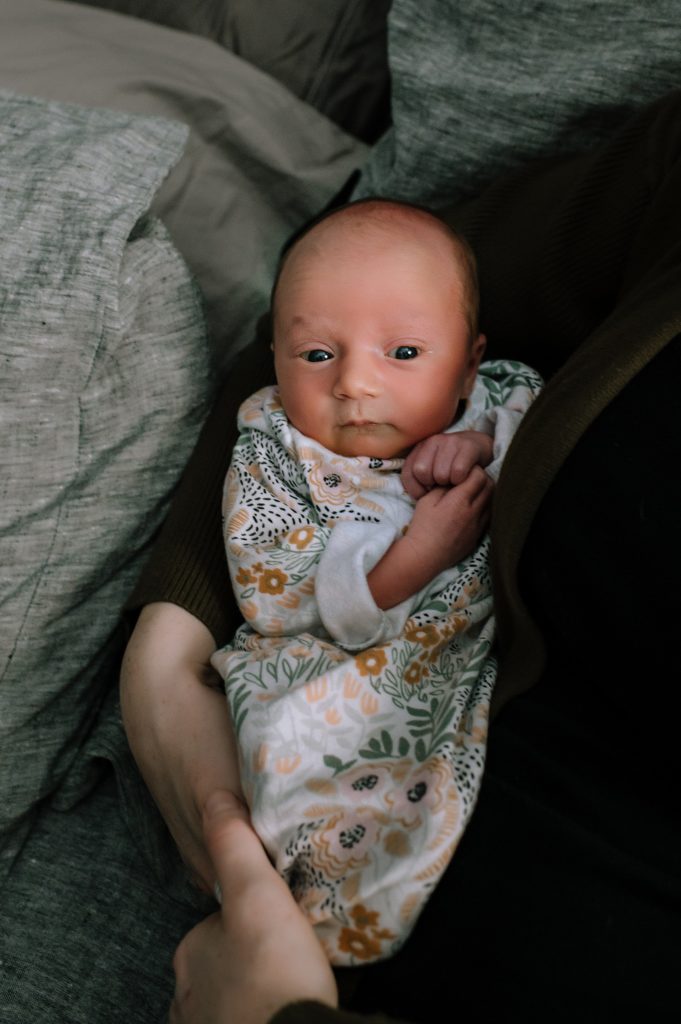 Tiny new baby snuggled in her mom's arms wearing a floral sleeper for this Michigan in-home newborn session.