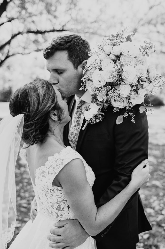 Groom kissing bride's forehead at their couples portraits in golden hour.