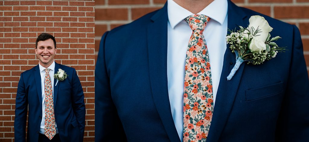 Groom in navy blue suit with coral floral tie and white flower boutonniere. 