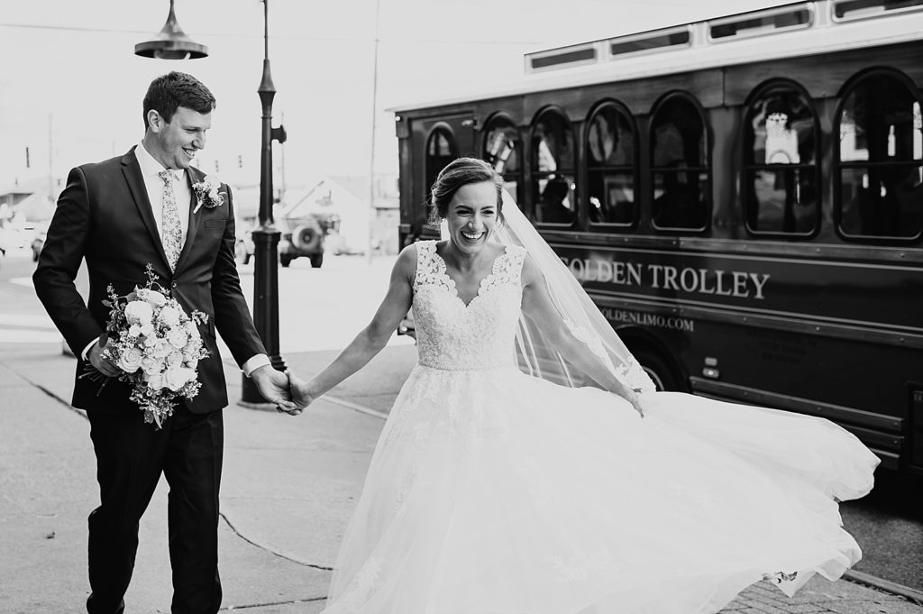 Bride and groom laughing on the sidewalk in front of a trolley by Michigan Wedding Photographer, Brittany Emerson.