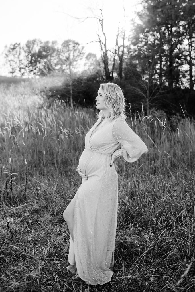 Pregnant woman holding her belly with her hand on her back in a field at White Lake in Michigan.