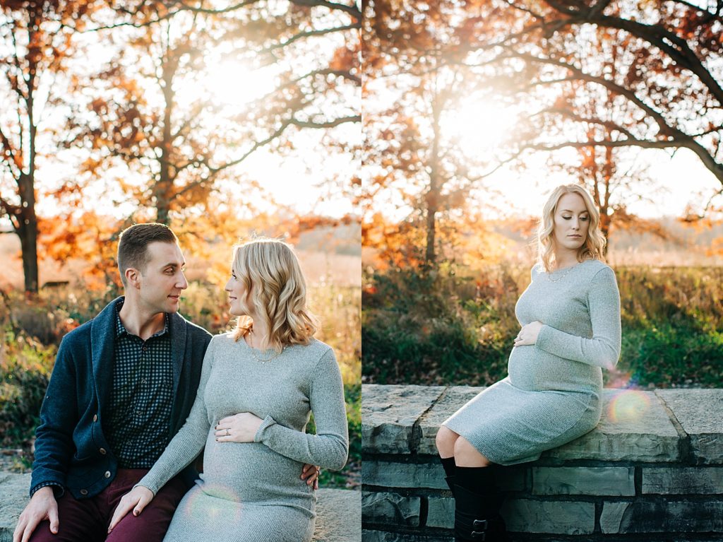 Pregnant woman in bodycon gray dress sitting on a stone wall at a park.