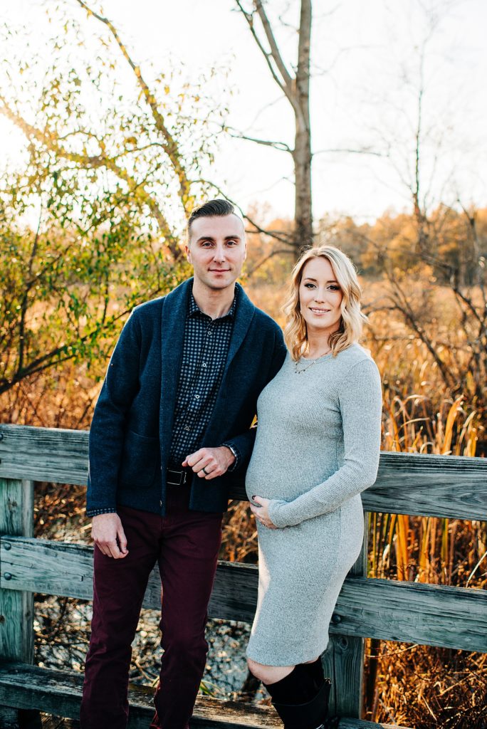 Pregnant couple posing by a fence in golden hour for a maternity session with Michigan photographer, Brittany Emerson. 