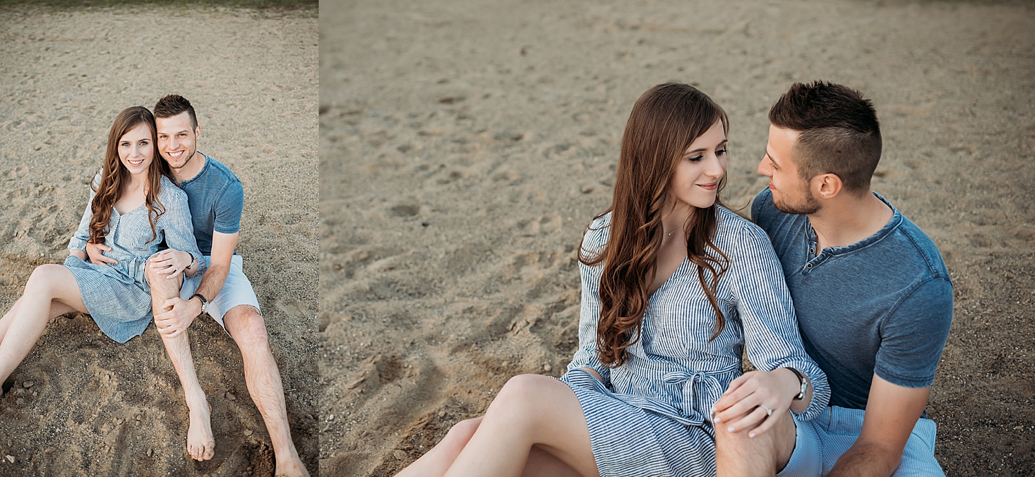 Couple sitting on beach during summer day engagement session wrapped in each other's arms